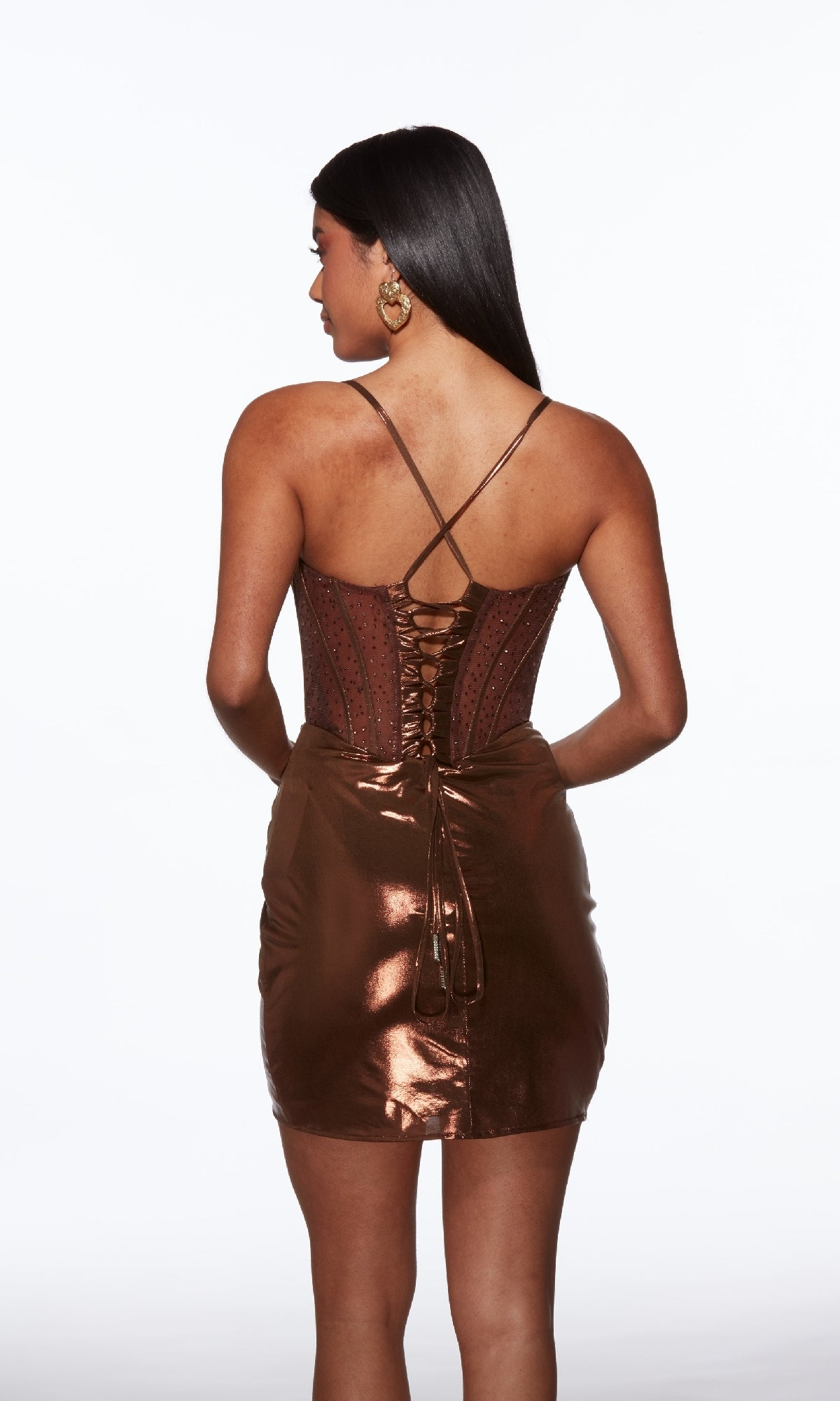 A woman faces away, modeling the Alyce 40103 short homecoming dress in metallic brown, featuring thin straps and a lace-up back, against a plain white background.